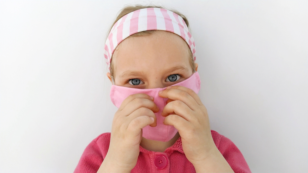 Little,girl,in,headband,wearing,protective,pink,fabric,mask,against